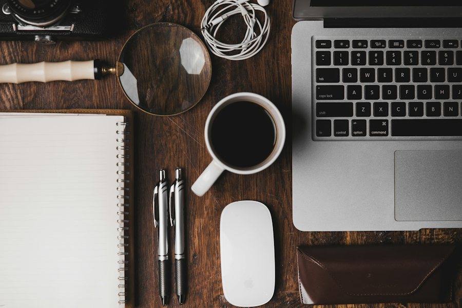 A dark desk with a tablet, notebook, glasses and a pen